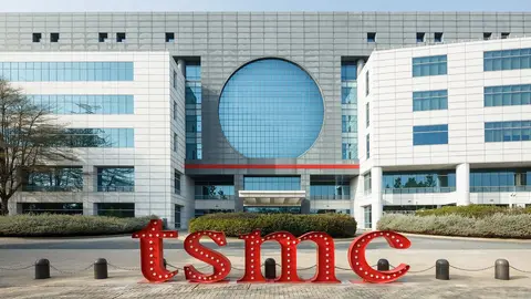 Fachada de prédio envidraçado da TSMC com letras vermelhas iluminadas 'tsmc' na frente, em dia claro