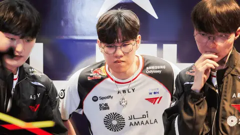 Jogadores da equipe T1 de uniforme branco e jaquetas pretas em evento de League of Legends, com o jogador do centro de óculos