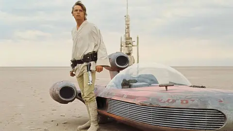 Luke Skywalker ao lado de um landspeeder em um deserto, cena de Star Wars