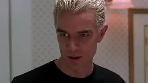 Spike, vampiro de Buffy, a Caça-Vampiros, em close com cabelo loiro platinado e camiseta preta