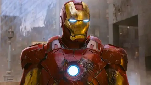 Homem de Ferro em cena de filme, com armadura vermelha e dourada e o reator arc azul brilhando no peito