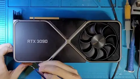 Mãos seguram uma placa de vídeo RTX 3090 Founders Edition sobre tapete azul de bancada, com ferramentas ao lado