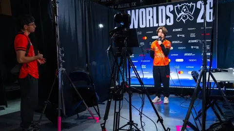 Jogador de League of Legends com microfone sendo entrevistado diante do painel do Worlds 2026, com patrocinadores ao fundo