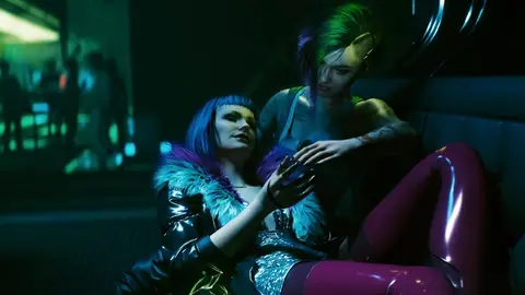 Duas personagens de Cyberpunk 2077, uma de cabelo azul com casaco de pelo e outra de cabelo verde e roxo, em ambiente neon noturno