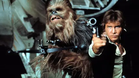 Han Solo aponta um blaster e Chewbacca ao lado dentro de uma nave, cena do filme Star Wars