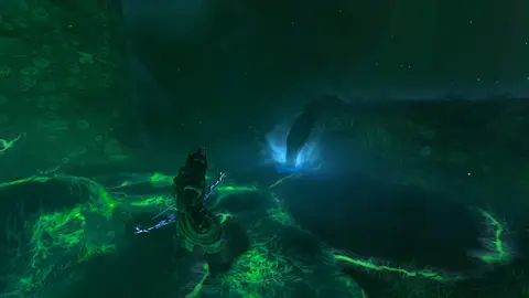 Personagem de armadura escura em área coberta de névoa verde, com uma fonte de luz azul ao fundo, em cena de jogo