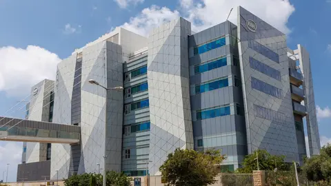 Prédio moderno da Intel com fachada de painéis metálicos e janelas de vidro, sob céu azul com nuvens