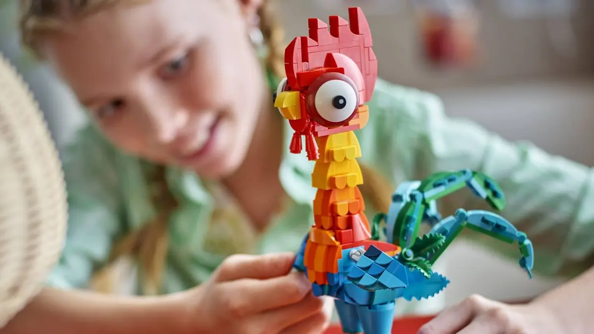 Menina sorri ao lado de uma galinha Heihei de LEGO, do set de Moana, com um pé de mão em primeiro plano