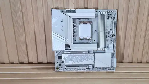 Placa-mãe Gigabyte Aorus branca com dissipadores, apoiada na vertical sobre fundo de madeira ripada
