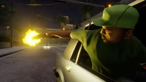 Protagonista de boné e camisa verdes dispara pistola pela janela de um carro em rua noturna, com clarão do tiro