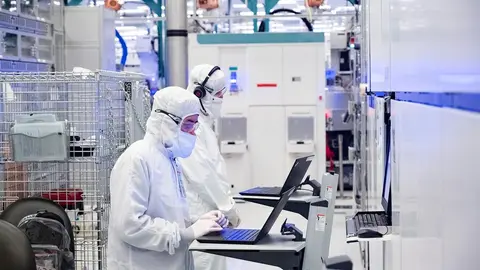 Dois técnicos de roupa branca de sala limpa trabalham com notebooks em uma fábrica de semicondutores