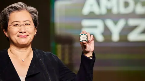 Mulher de cabelo grisalho e óculos segura um processador Ryzen em palco, diante de tela com o nome AMD Ryzen