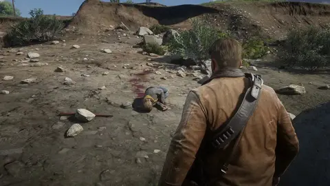 Personagem de Red Dead Redemption 2 de costas, de jaqueta marrom, olhando um corpo caído em terreno rochoso com sangue
