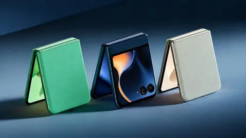 Três smartphones dobráveis Motorola Razr 60 em verde, azul-marinho e bege, apoiados em fundo azul-acinzentado