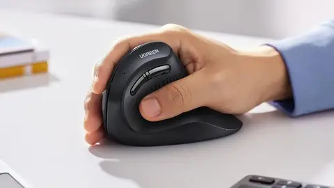 Mão segurando um mouse vertical preto da UGREEN sobre uma mesa clara