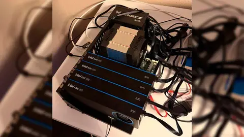 Quatro placas Intel Arc B70 empilhadas em estrutura preta sobre mesa, com cooler de CPU e cabos de alimentação ao redor