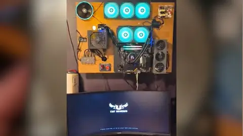 PC montado sobre placa de madeira fixada na parede, com coolers RGB e monitor TUF Gaming abaixo