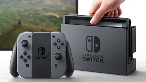 Nintendo Switch com Joy-Con cinzas no grip ao lado da base, com uma mão encaixando o console