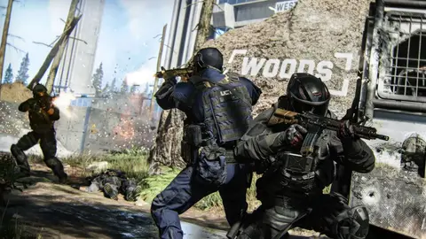 Dois operadores táticos com rifles em combate em área externa, com caminhão e muro de concreto ao fundo, em captura de jogo