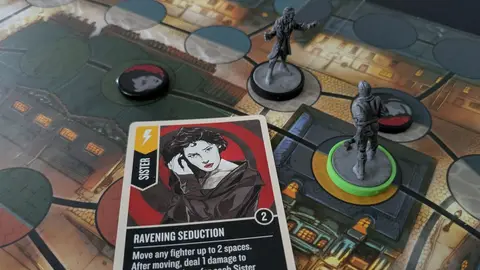 Miniaturas cinzentas e uma carta 'Ravening Seduction' sobre tabuleiro de cidade vitoriana, em foto real do jogo de tabuleiro