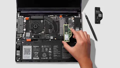 Mão encaixa módulo de memória RAM em notebook Framework aberto, com chave de fenda e bateria ao lado