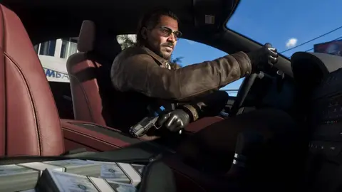 Homem de óculos e casaco marrom dirige carro de luxo com pistola no colo e maços de dinheiro no banco, cena de GTA 6
