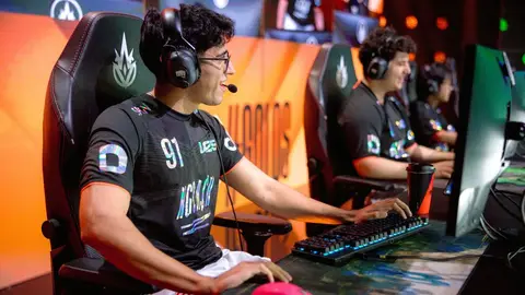 Jogador de LoL de camisa preta, headset e número 91, em evento de esports com teclado iluminado ao fundo.
