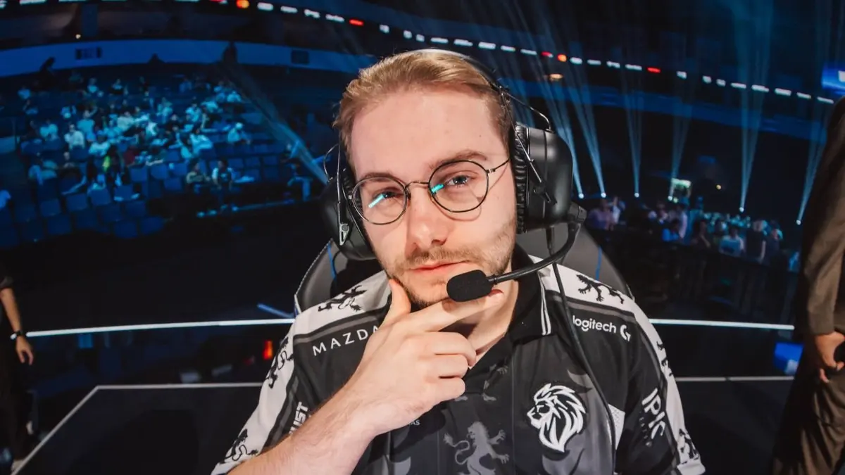 Jogador de e-sports com headset e camisa de equipe com logo de leão, em arena com plateia ao fundo