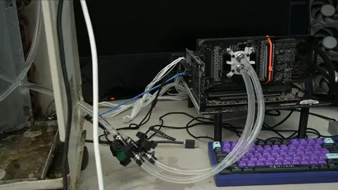 Placa de vídeo com bloco de água e mangueiras transparentes ligada a um radiador, em bancada com teclado roxo