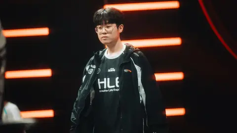 Jogador da HLE de jaqueta e camiseta da Hanwha Life Esports caminhando em palco de evento com luzes laranja